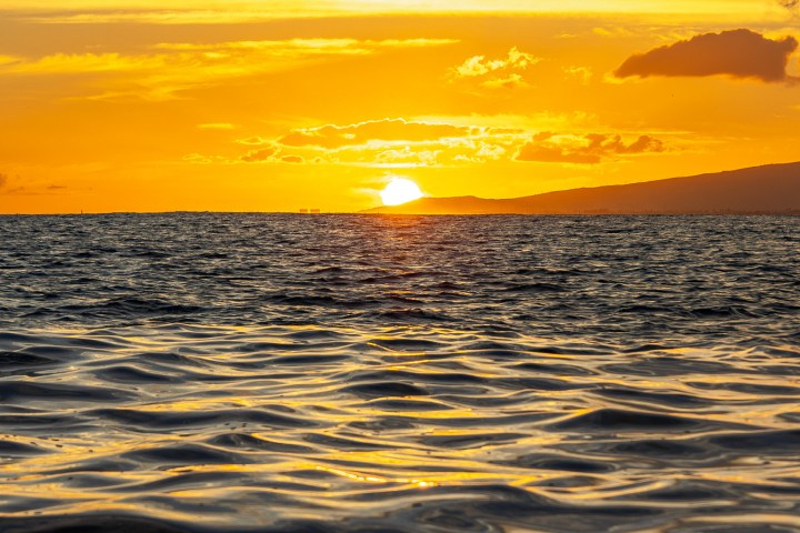 Sunset over ocean with golden sky and rippling waves in foreground.
