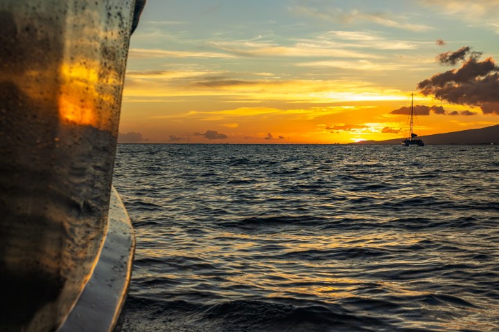 Boat on water at sunset with clouds and sailboat in distance.