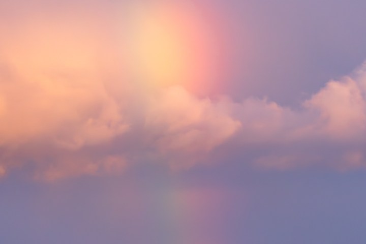 Calm ocean with a faint rainbow and colorful clouds in the sky.