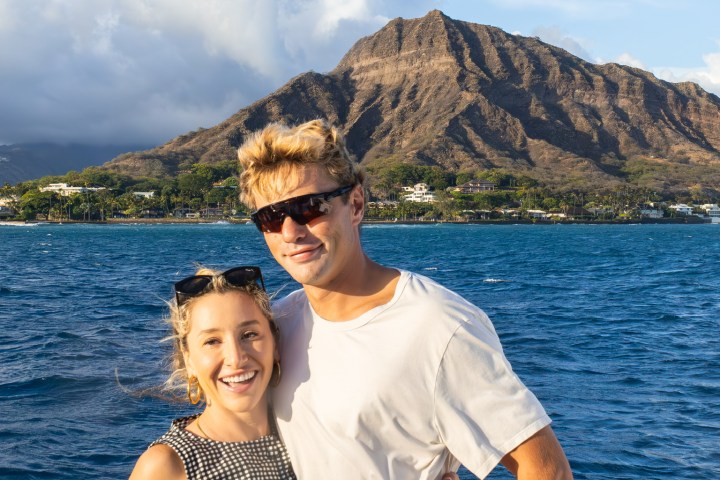 Couple on a boat smiling with a mountain and ocean background.