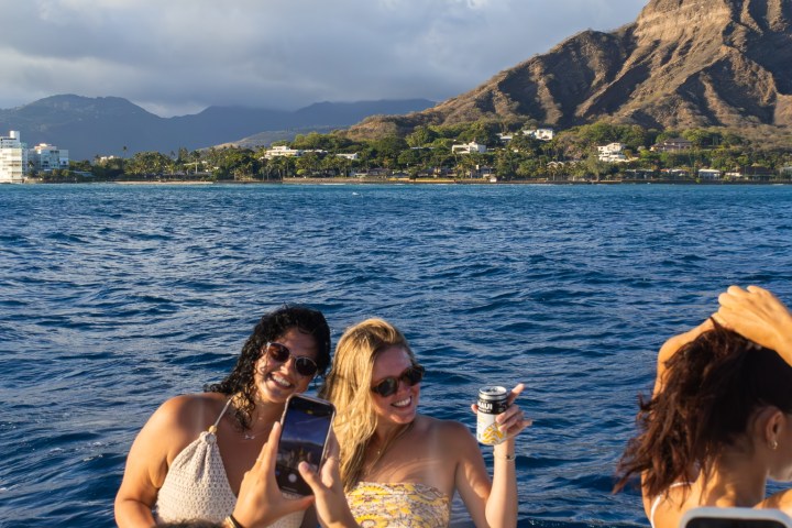 People on a boat taking photos with mountains and ocean in the background.