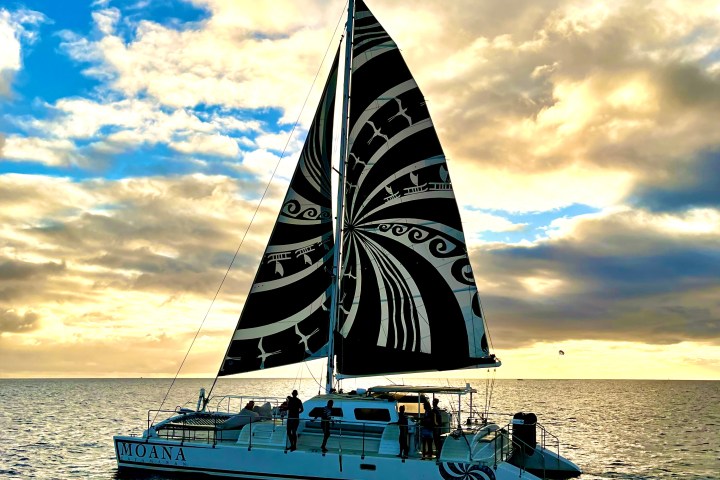Sailboat with ornate sail on the open sea at sunset.